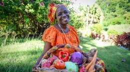 A woman in Dominica sits in front of a basket of food.
