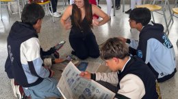 Una voluntaria dirige una actividad sobre ciudadanía digital con varios estudiantes, reunidos en el suelo con periódicos y teléfonos móviles.