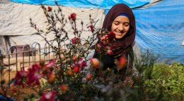 A young woman in Iraq stands in front a small plant.