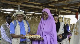 A woman in Nigeria holds a carton of eggs, surrounded by aid workers and local community members.