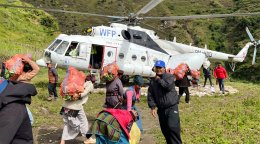 People carry bags of food in Nepal in front of a helicopter.