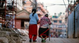 An elderly woman and younger woman in Nepal walk together.