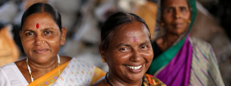 Three women in colorful saris stand in a triangle formation. 