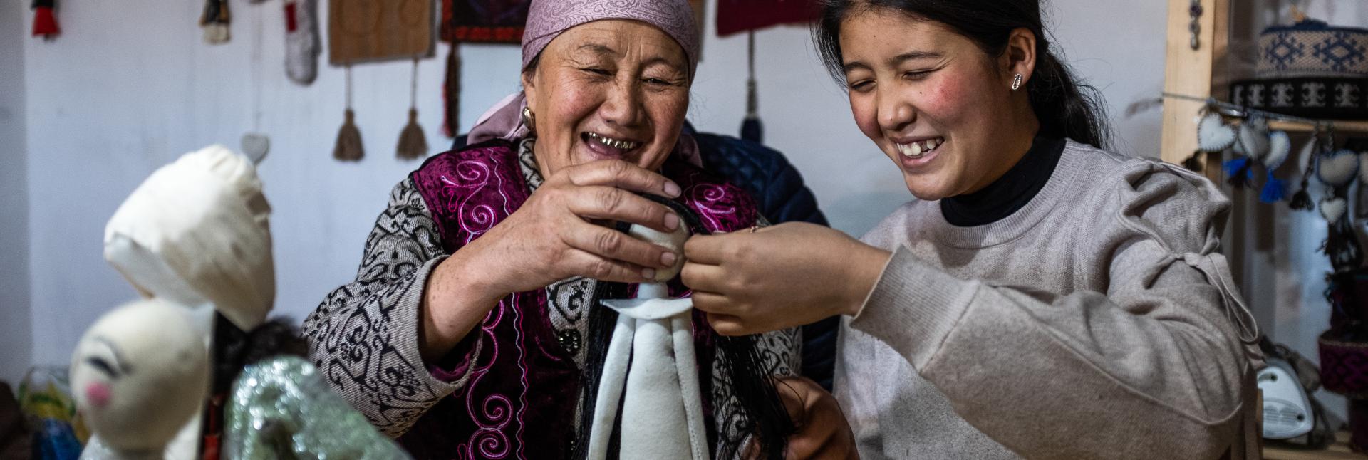 Two women smile while they put together a doll. 