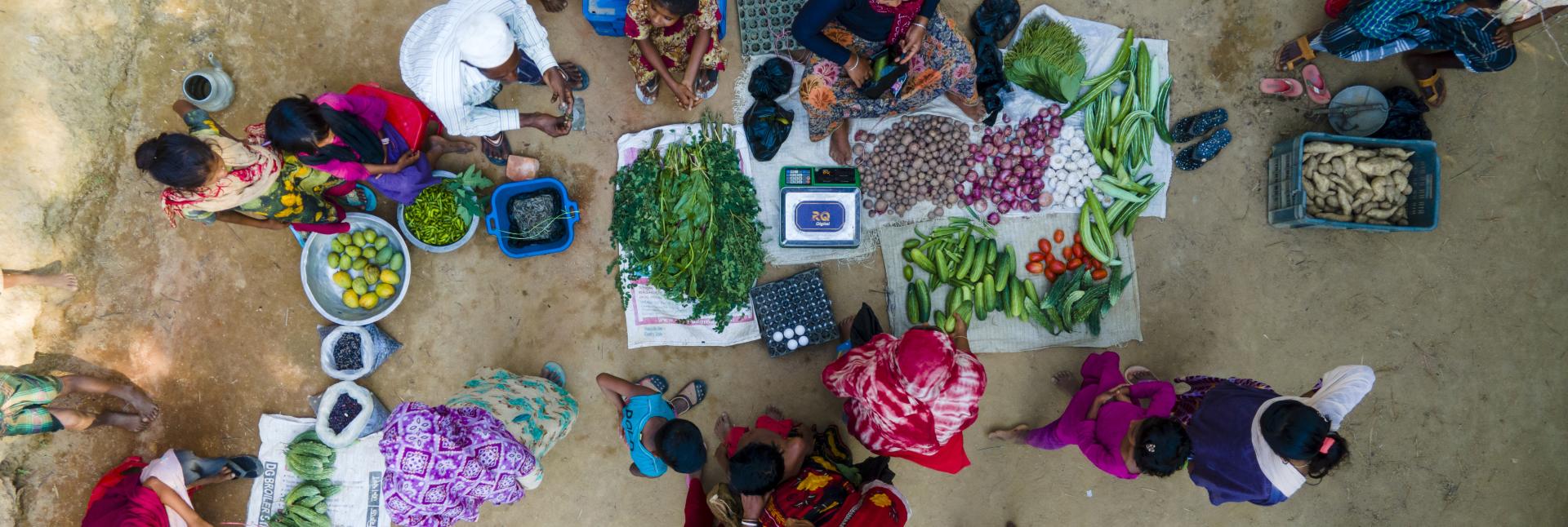People sit on the street, amid colorful vegetables.