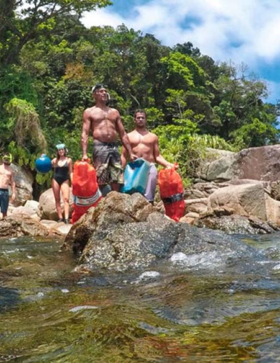 Four people, in bathing suits and with equipment in their hands, stand on rocks near the ocean. 