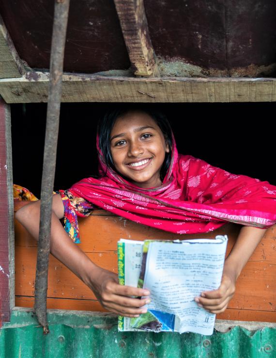 Girl in a pink dress holding a book peeping through a window