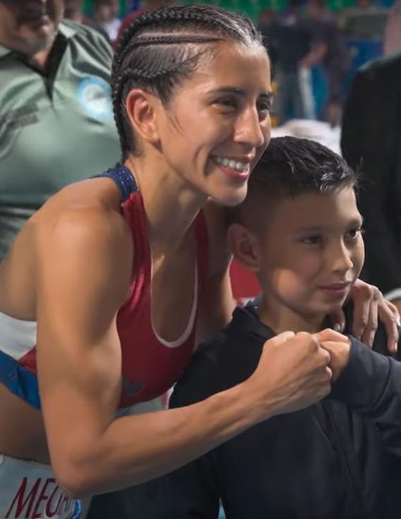 A female boxer embraces a young fan with a fist bump.