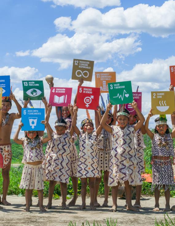مجموعة من الأطفال يرتدون ملابس تقليدية يحملون لوحات تُظهر أهداف التنمية المستدامة.