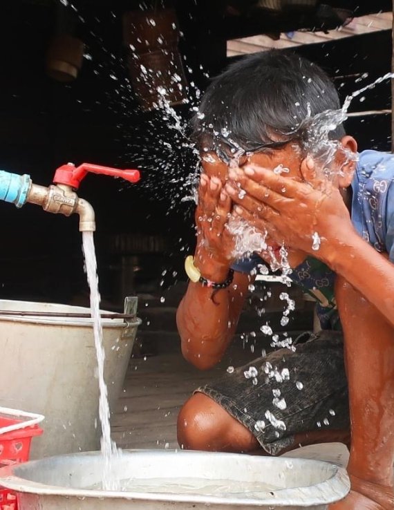 A child in Lao PDR splashes water on his face.