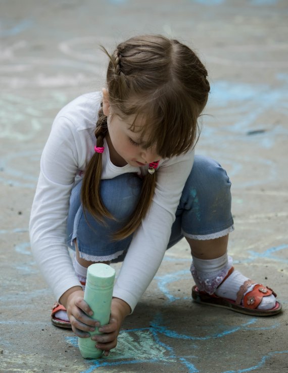 A girl in Moldova draws on the ground with chalk.