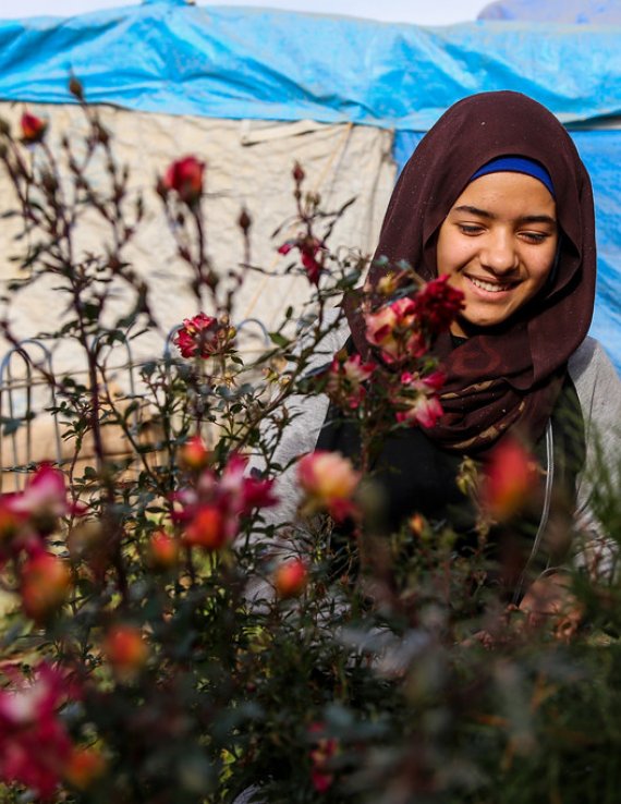 A young woman in Iraq stands in front a small plant.