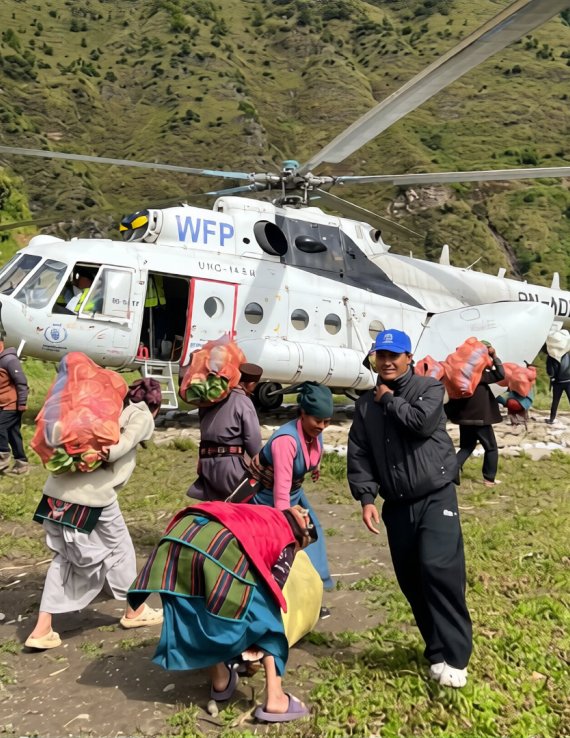 People carry bags of food in Nepal in front of a helicopter.
