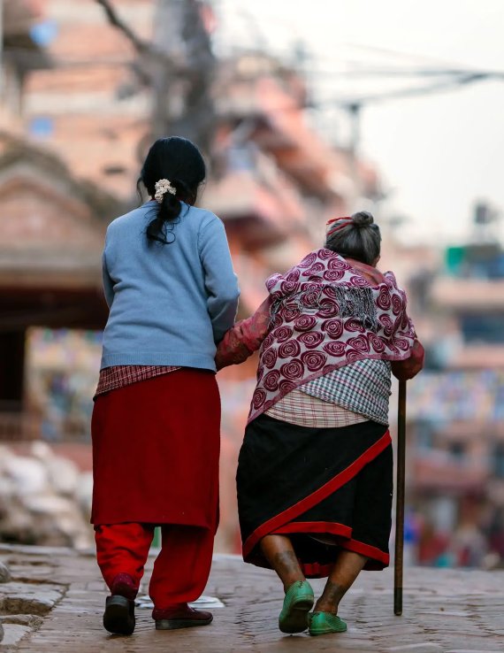 An elderly woman and younger woman in Nepal walk together.