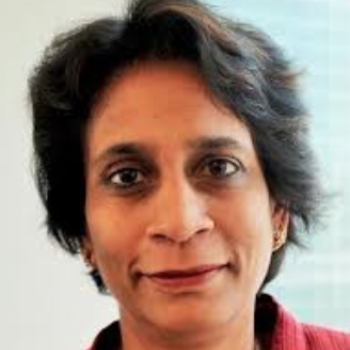 A woman in a red suit and brown short hair smiles and faces the camera.