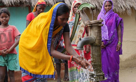 Mujeres y niñas de la zona esperan para lavarse las manos en la bomba de agua.