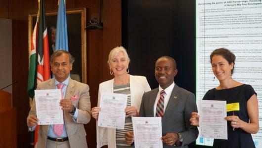All four signatories smile as they stand holding their signed commitments