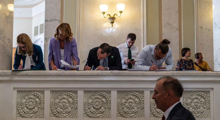 Plusieurs personnes sont penchées sur un parapet et signent des documents à l'intérieur d'un bâtiment à l'architecture classique.