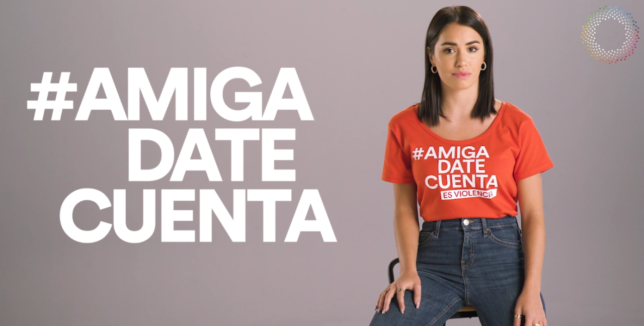 Shows a woman sitting looking at the camera. She's wearing a t-shirt that reads  #Friendrealizewhatishappening and the text in big bold letters again to the left of her with the Spotlight Initiative logo just above her on the right. 