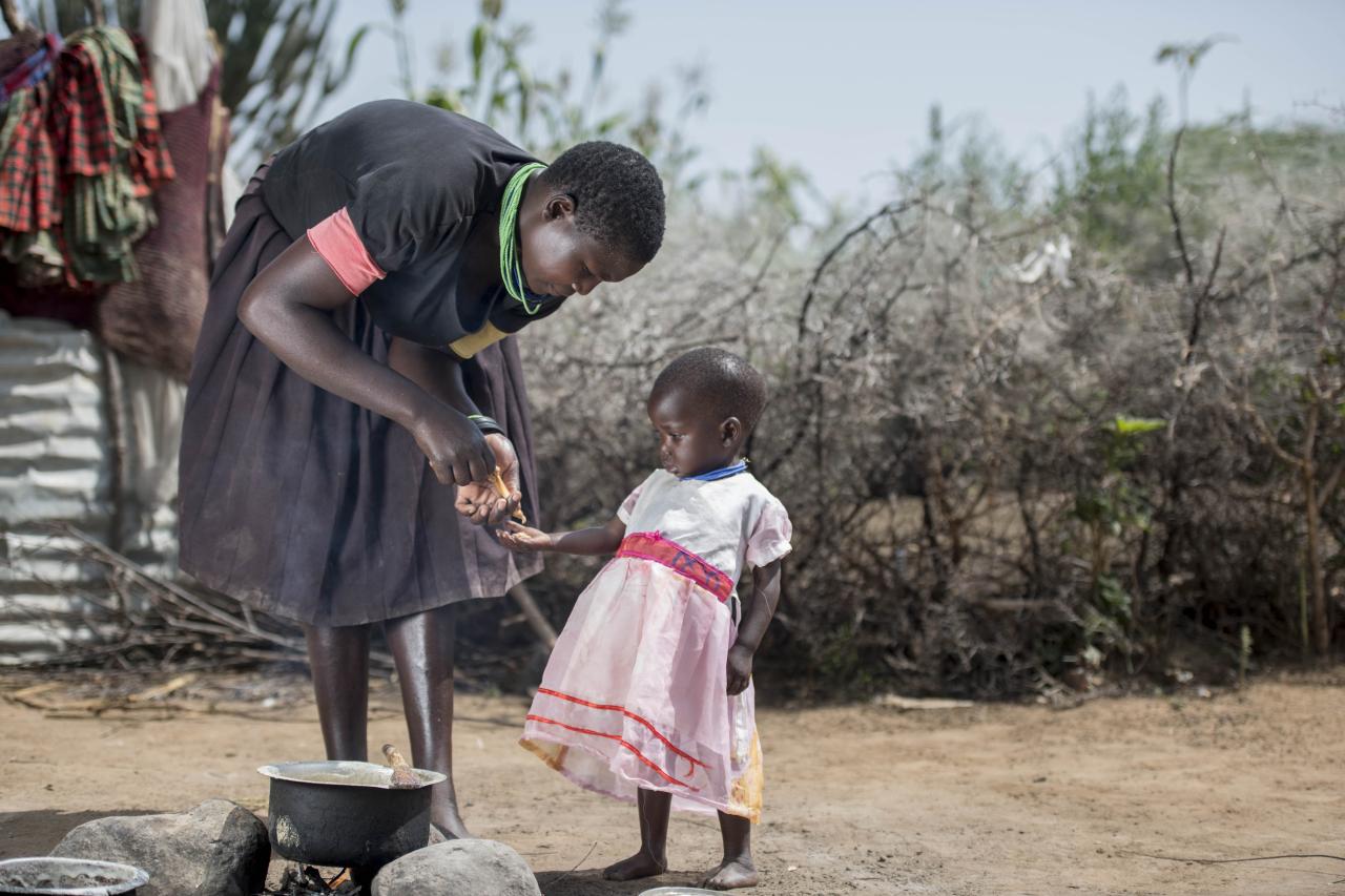 Photo shows a mother teaching her young toddler to cook.