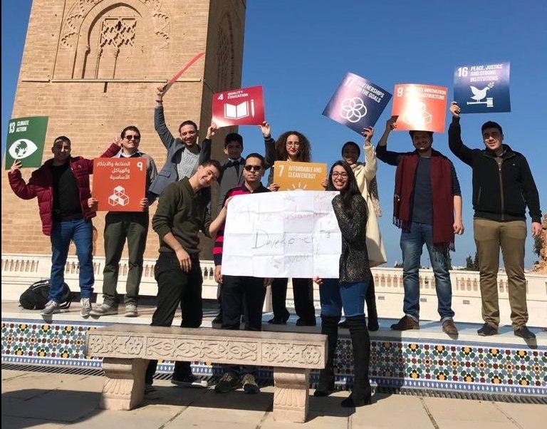 Young people pose towards the camera happily holding SDG signs.
