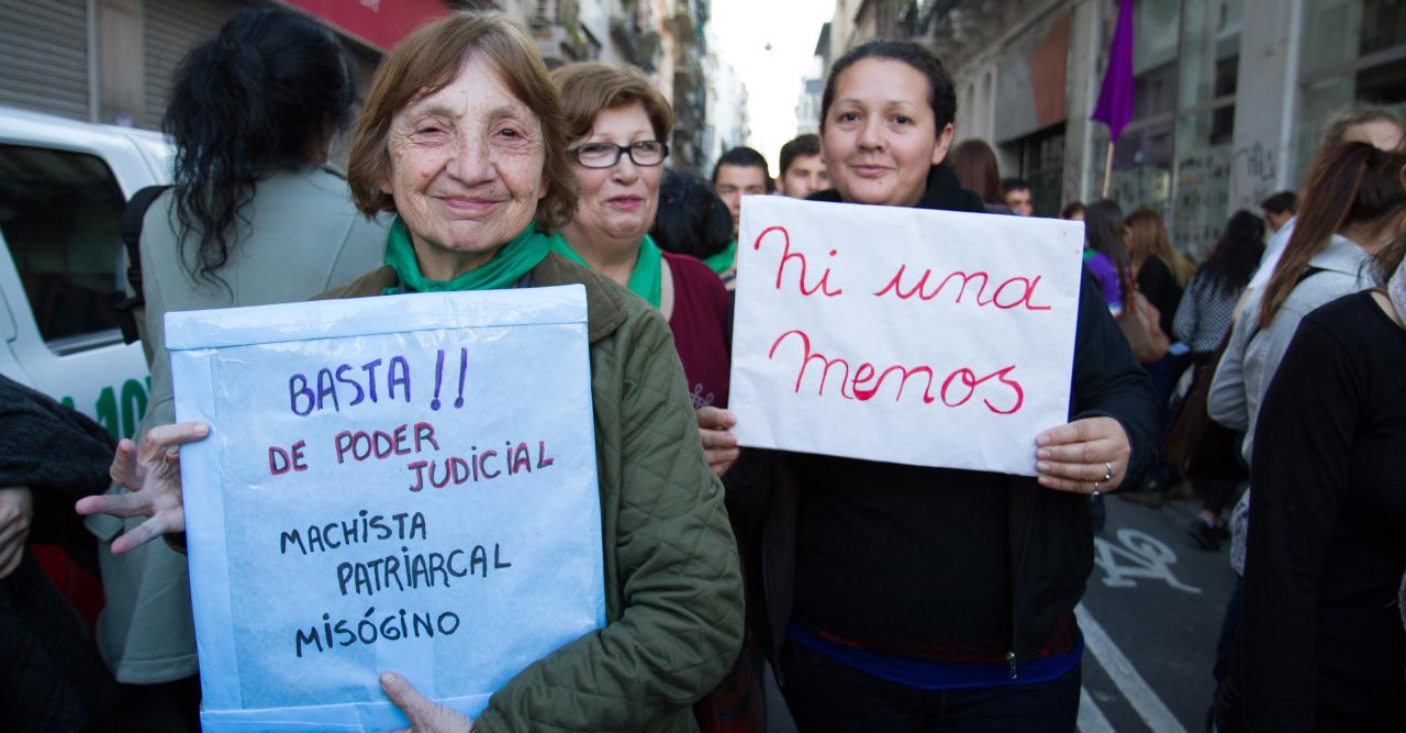 Dos manifestantes sostienen carteles, sonriendo para la cámara.