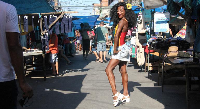 Shows young person smiling and posing at the camera, while at a local market.
