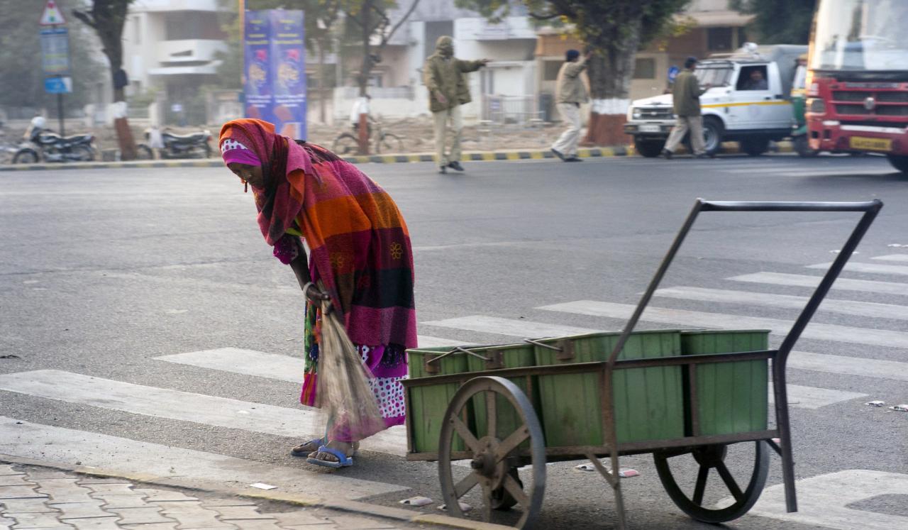 Una mujer ataviada con un velo que cubre la cabeza, el pecho y le llega hasta las rodillas, tira de una carrucha verde sobre un paso de peatones, en la calle.