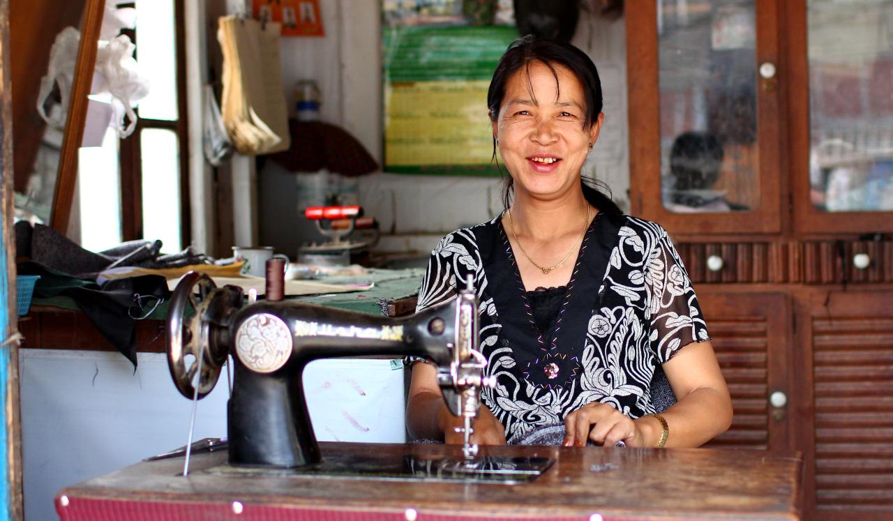 A curbside seamstress in Chin State, Myanmar uses a foot pedal to power her sewing machine.