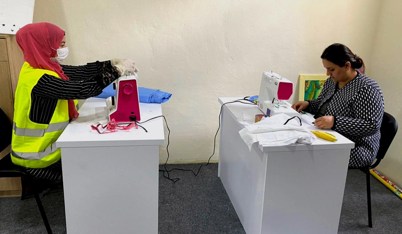 Two women sew protective masks.