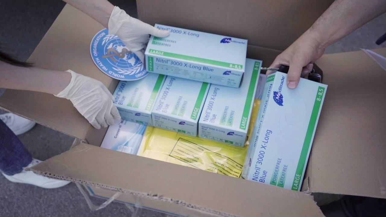 Photo shows close-up of hands removing lifesaving supplies from a box donated by the World Health Organization.
