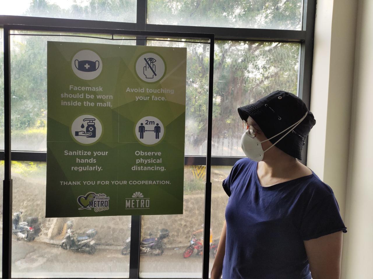A woman stands near an awareness raising sign about safety precautions citizens should take to prevent them from catching COVID-19.