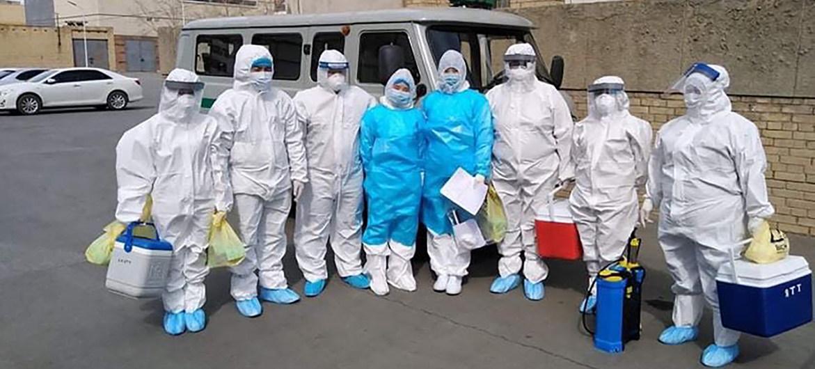 Des femmes et homme se tiennent les uns à côté des autres , face caméra, devant une camionnette. Ils portent chacun un équipement de protection individuelle de la tête aux pieds.
