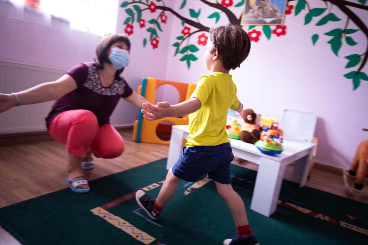 A caregiving wearing a protective face masks prepares to give a social distanced hug to one of the young residents of the programme.