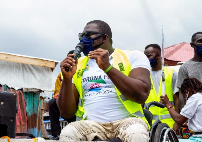 Una foto de George Wyndham, medallista paralímpico de Sierra Leona, en su silla de ruedas y hablando por un micrófono para dirigirse a una multitud
