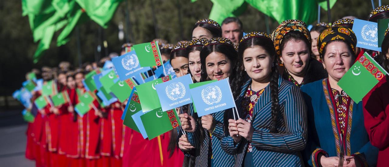Unas jóvenes sostienen las banderas de la ONU y de Turkmenistán mientras celebran la inauguración de la Casa de la ONU.