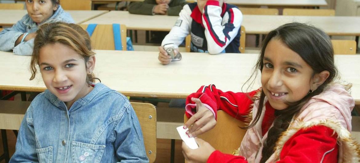 Dans une salle de classe, des enfants roms sont assis et regardent l'appareil photo en souriant.