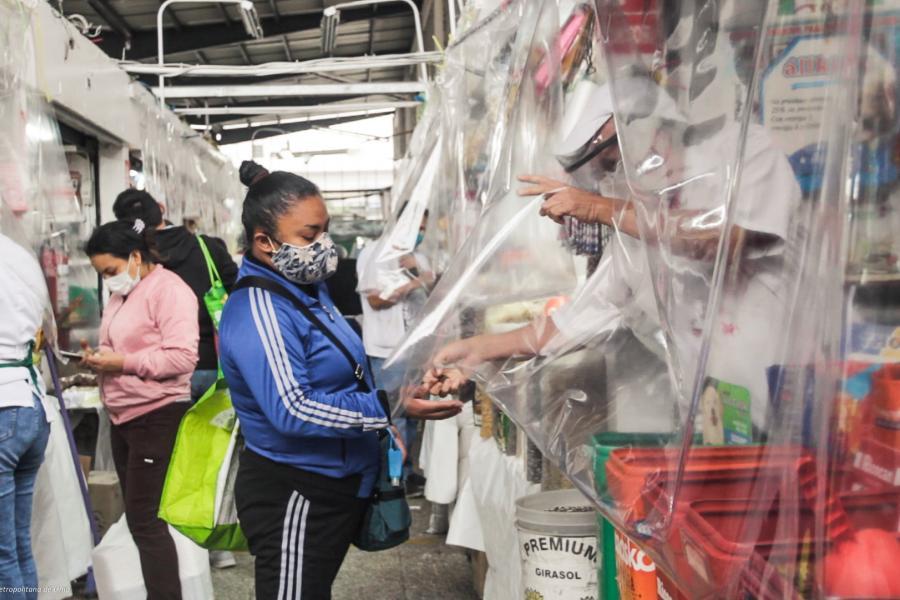 A vendor behind a clear plastic shield provides change to one of his customers.