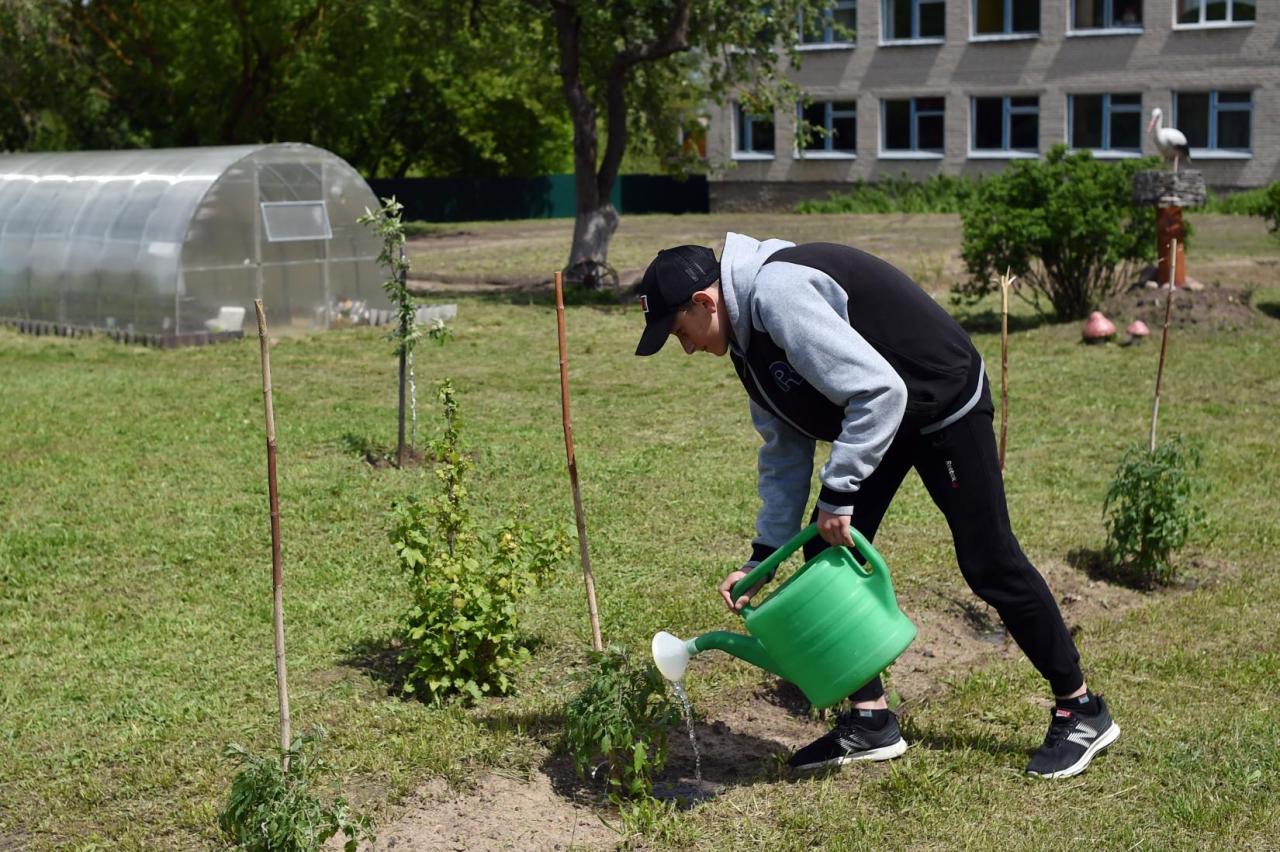 A young man waters the plants outside the school.