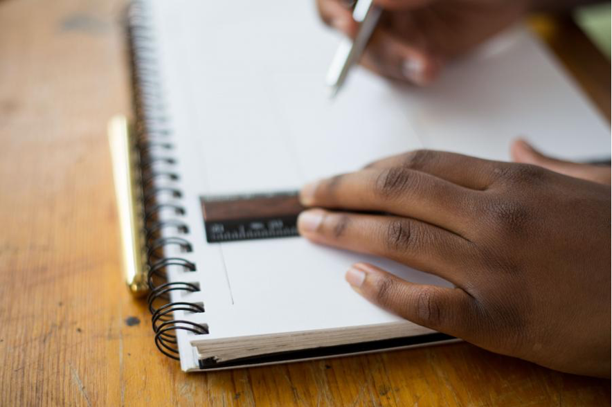 Close up a child's hands holding a ruler on a pad and a pen in the other hand.