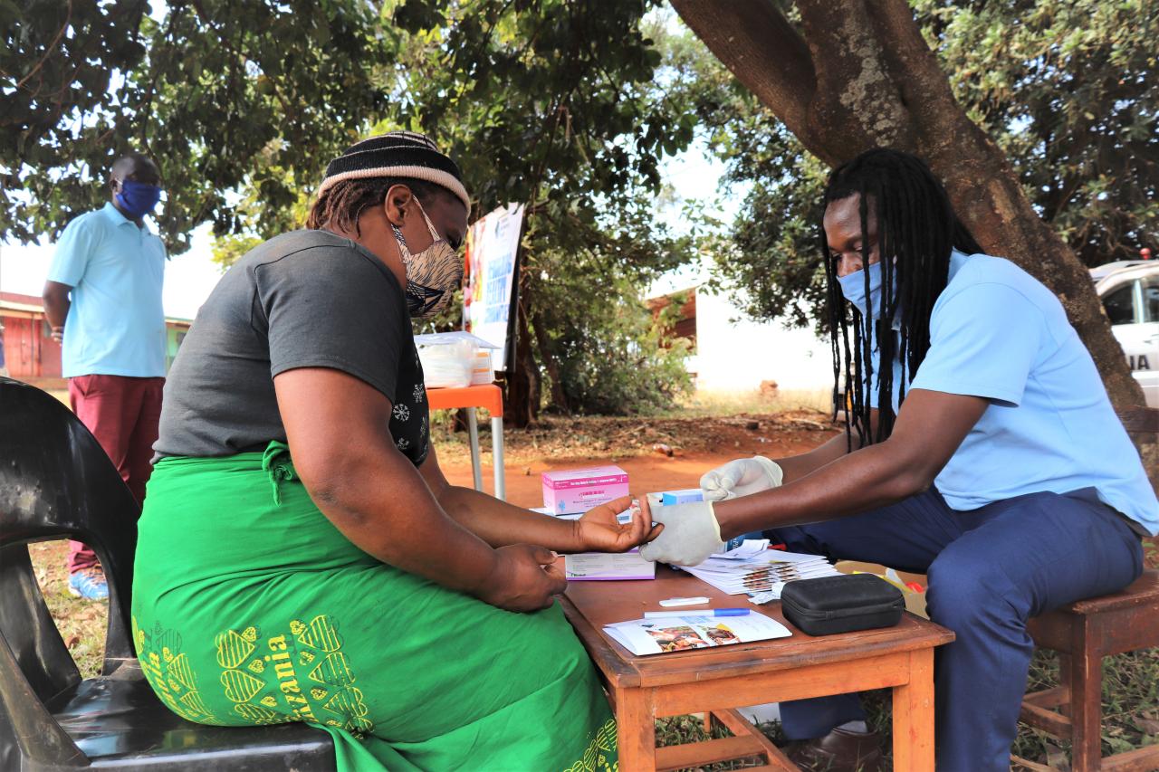 A healthcare worker tends to a woman at a desk stations outside as a man awaits his turn.
