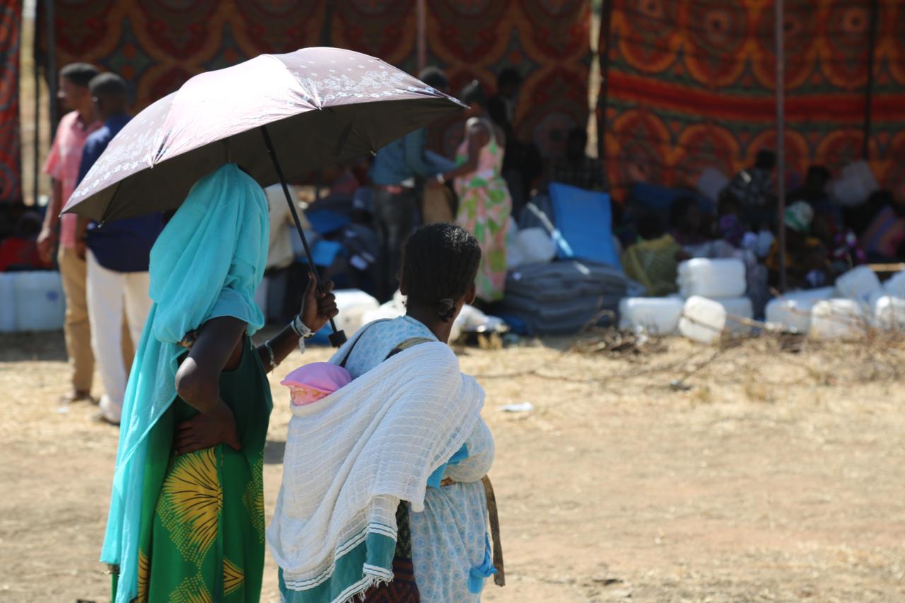 A refugee woman and children walk under an umbrella at the camp.