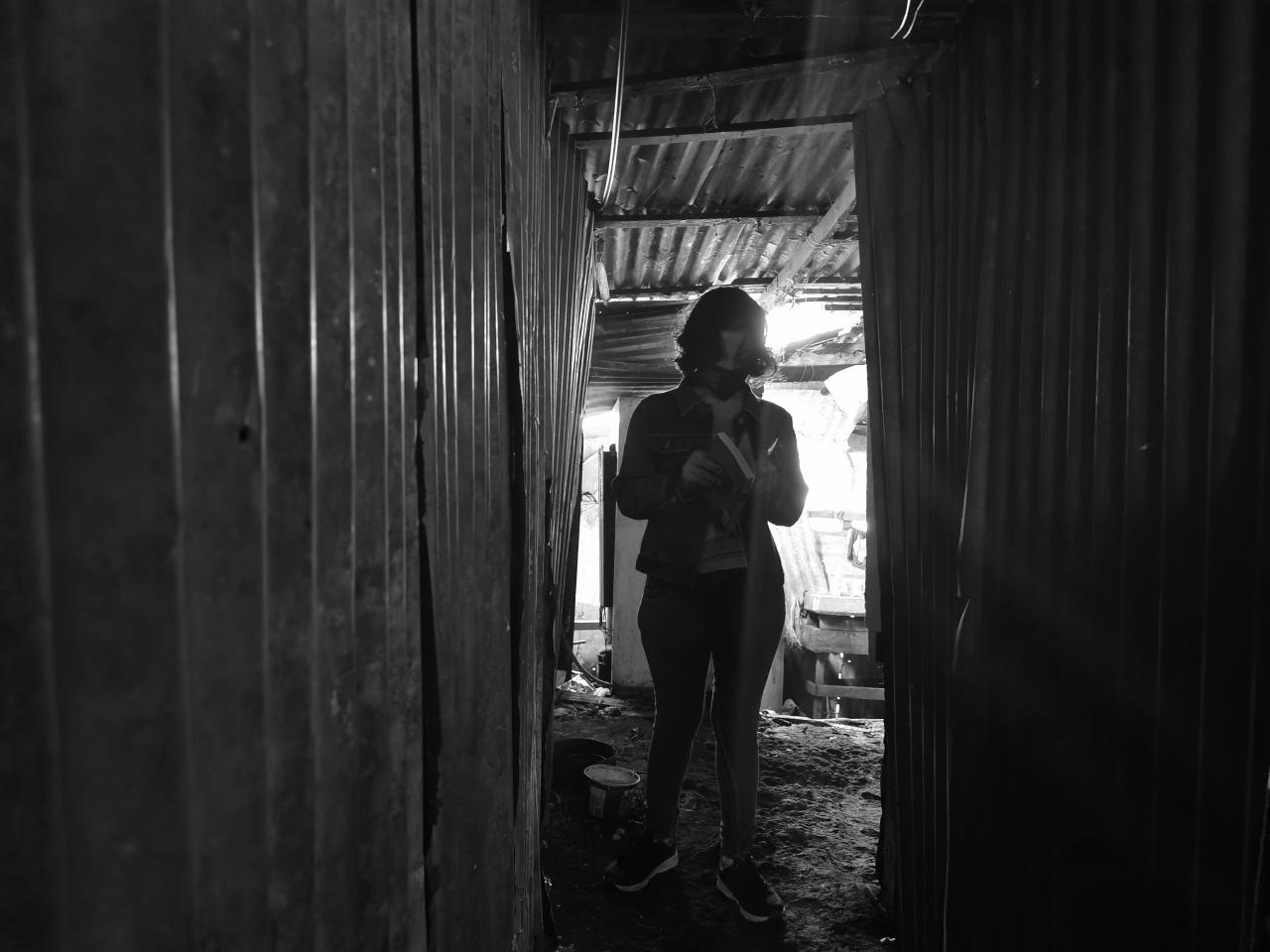 Lilith stands at the end of a passageway as she looks down at her book.