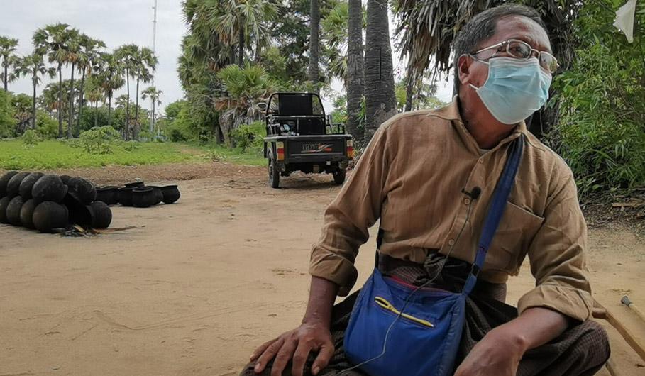 U Cho wearing a face mask sits down in front of the farmland.