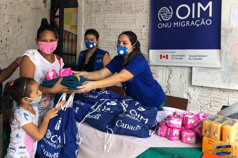 IOM staff a distribution station cheerfully hand over essential supplies to a mother and daughter.