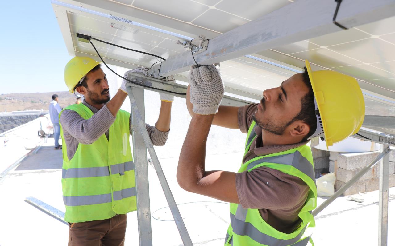 Dos hombres con cascos y chaquetas reflectantes están trabajando en paneles solares.