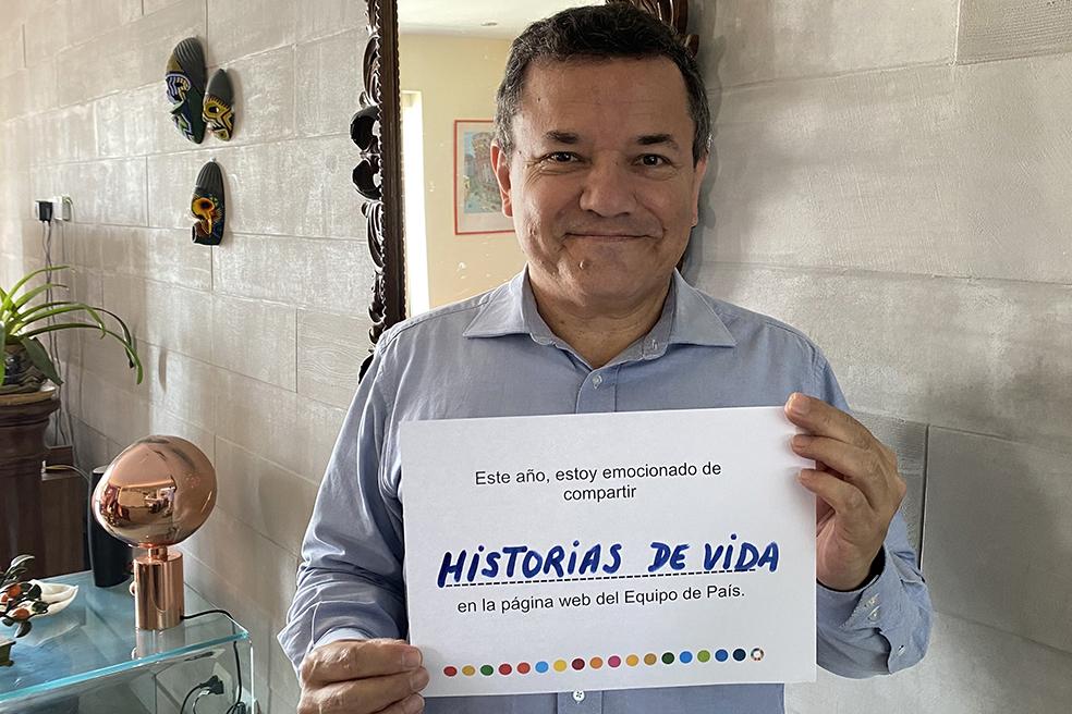 A man smiles sweetly at the camera as he holds up a small sign that shares his vision of the site for the next year, in Spanish.