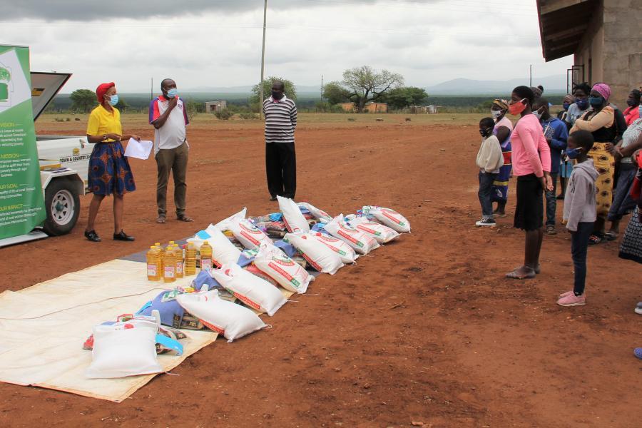 UN staff and families, wearing face masks, all stand outside on the opposite sides of a row of supplies placed in the middle.