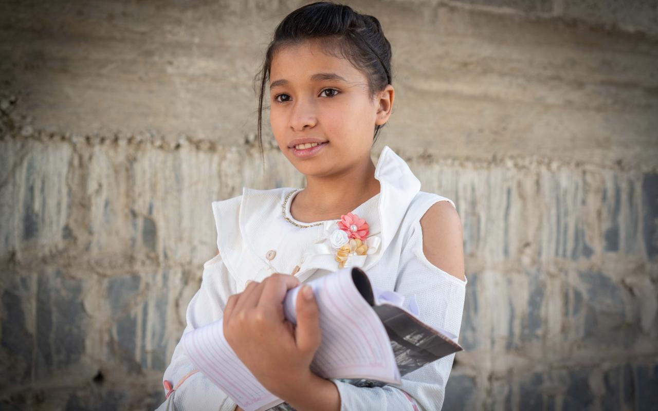 Amina, de 12 años, mira fuera de la cámara mientras sostiene con orgullo su cuaderno.