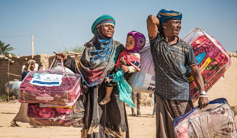 Una familia desplazada en Marib, Yemen, lleva un paquete de ayuda para el invierno de regreso a su refugio.